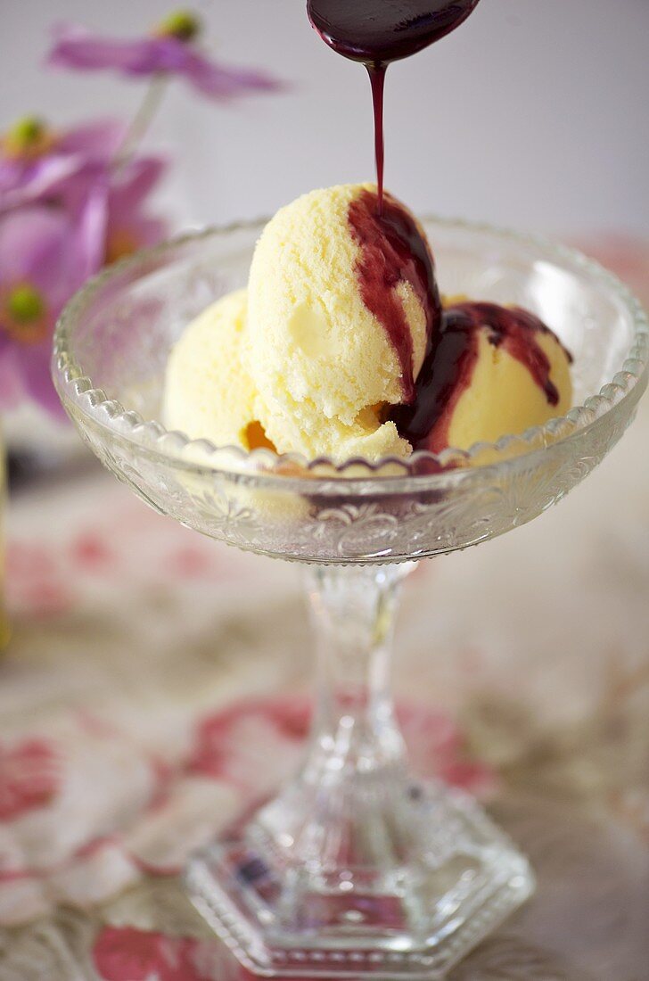 Pouring raspberry and red wine sauce over vanilla ice cream