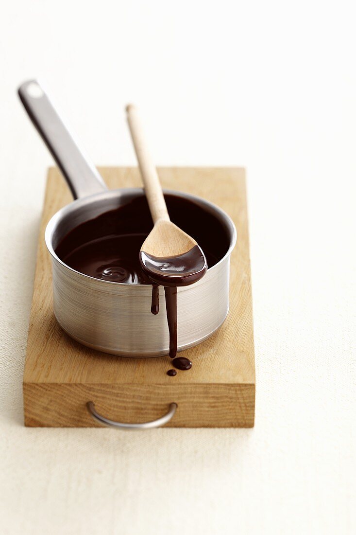 Schokoladensauce fließt von einem Holzlöffel & Topf