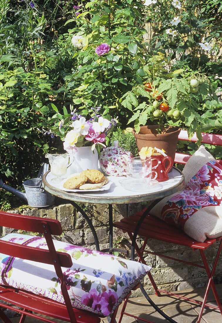 Gartentisch mit Teegeschirr, Gebäck, Blumen und Pflanzen