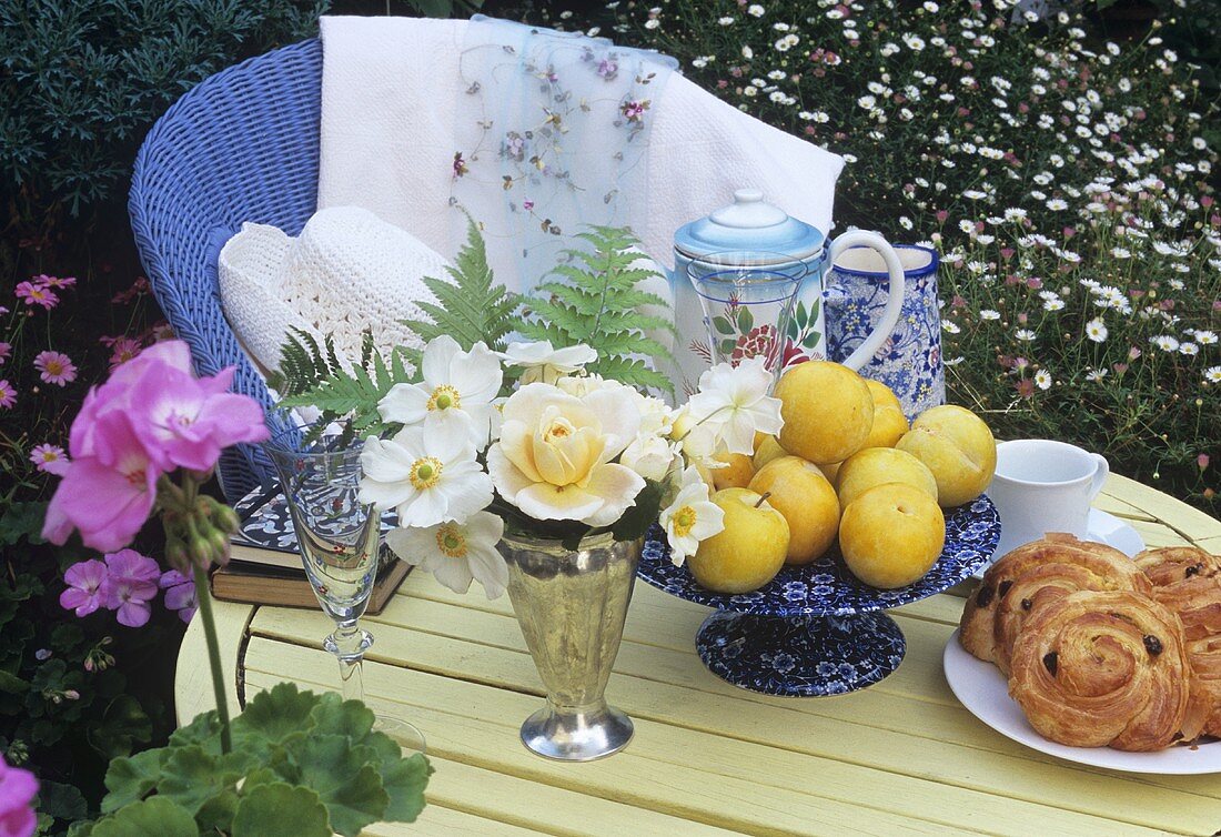 Gartentisch mit Blumen, gelben Pflaumen, Rosinenschnecken