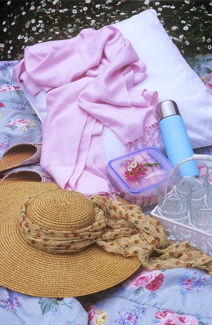 Picknickdecke mit Strohhut, Gläsern und Thermosflasche