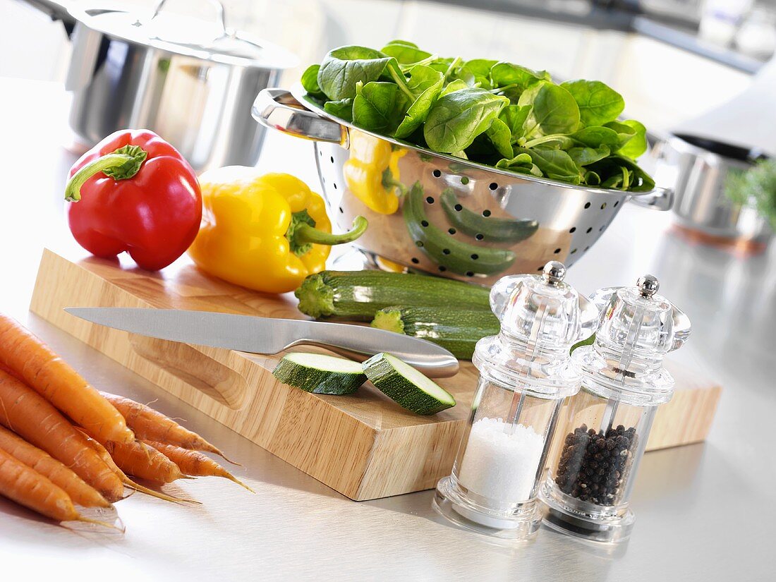 Küchenszene mit Gemüse, Messer, Sieb, Pfeffer- & Salzstreuer