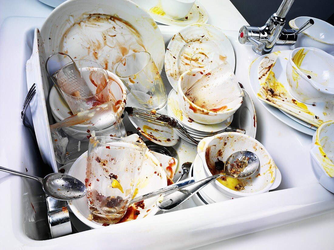 Dirty crockery and cutlery in and beside kitchen sink