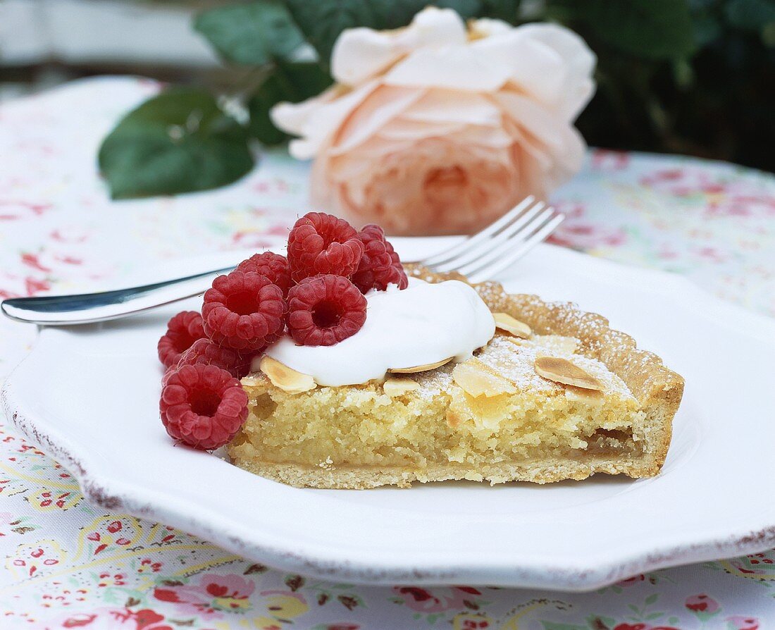 A piece of almond tart with raspberries and cream