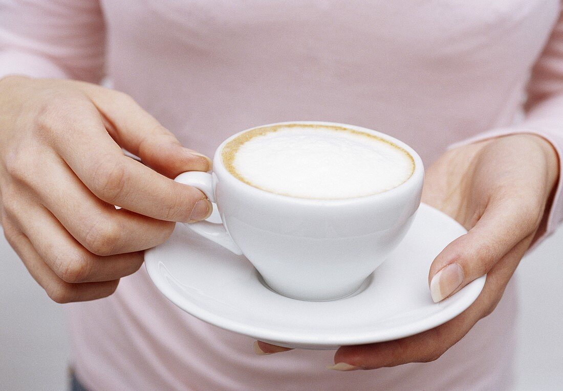 Frau hält eine Tasse Cappuccino (Bildausschnitt)