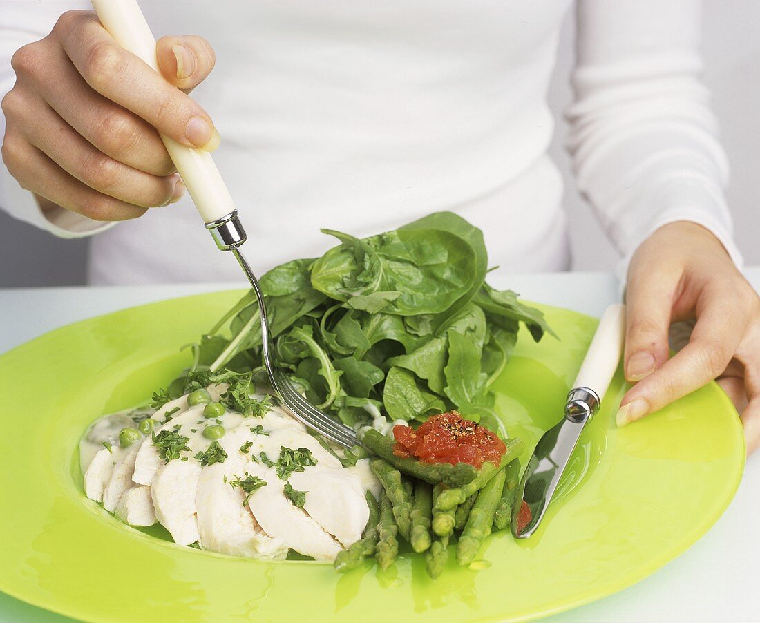 Frau isst Heilbutt mit Spargel und Spinatsalat