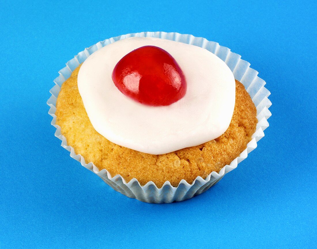 Iced cupcake with cherry on blue background