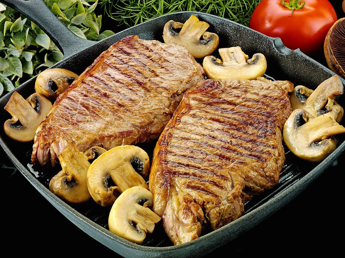 Two beef steaks with mushrooms in a grill pan
