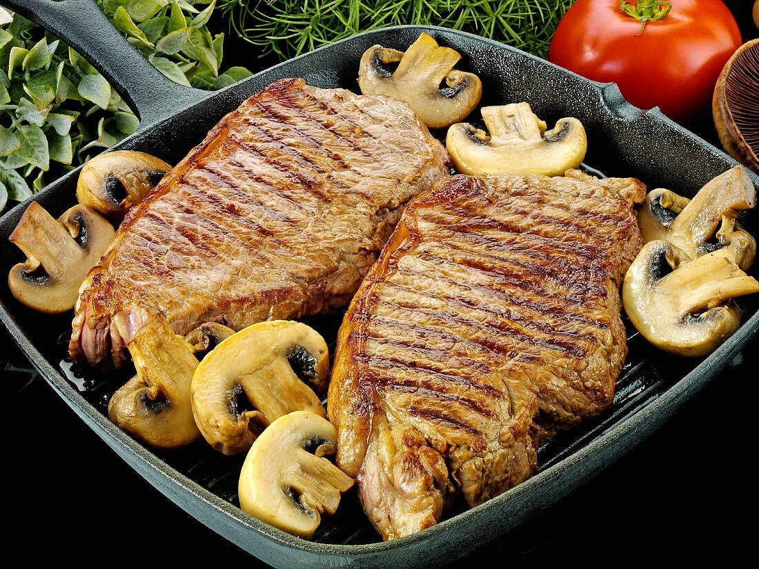 Zwei Rindersteaks mit Pilzen in einer Grillpfanne