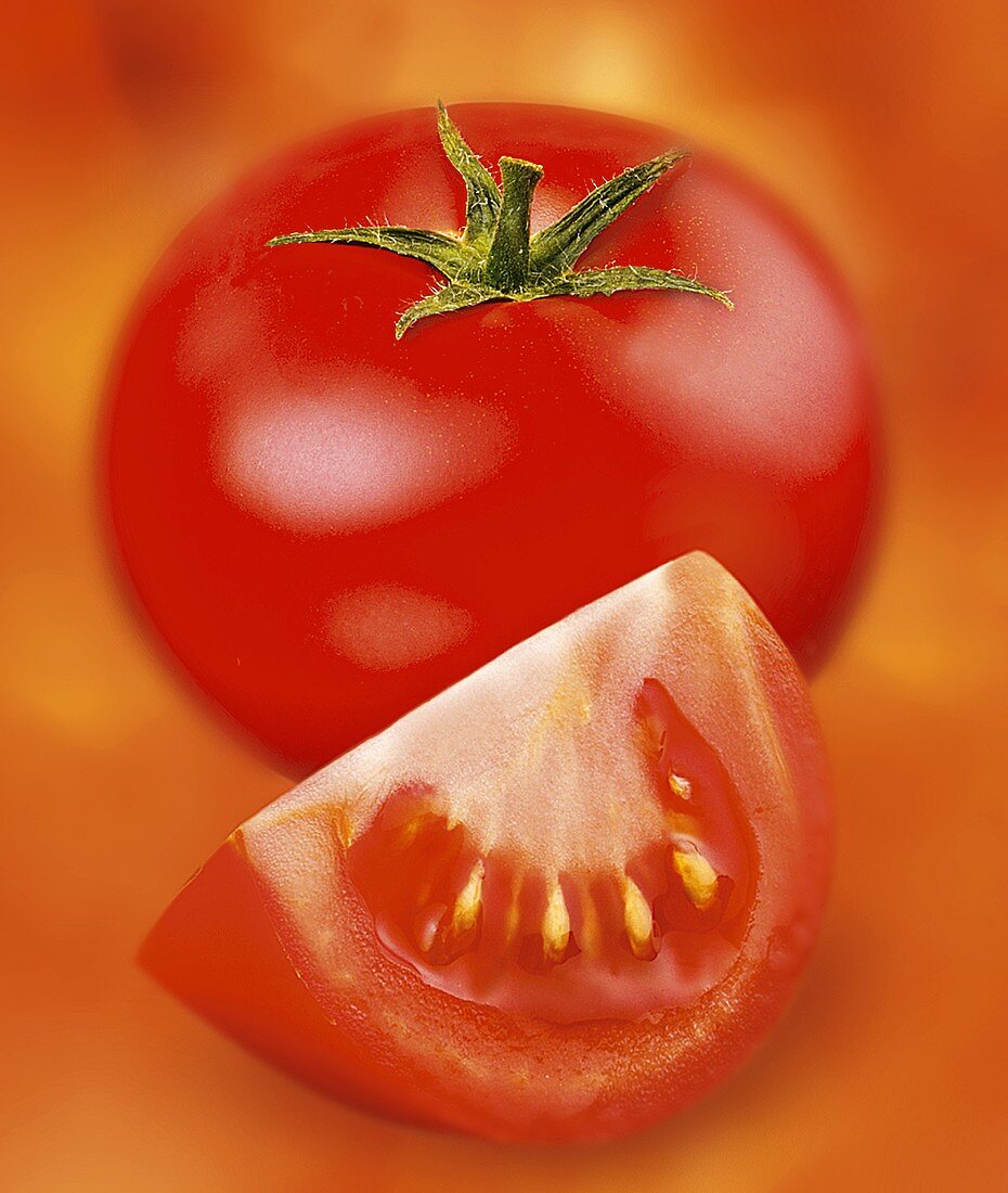 Tomato and wedge of tomato against red background