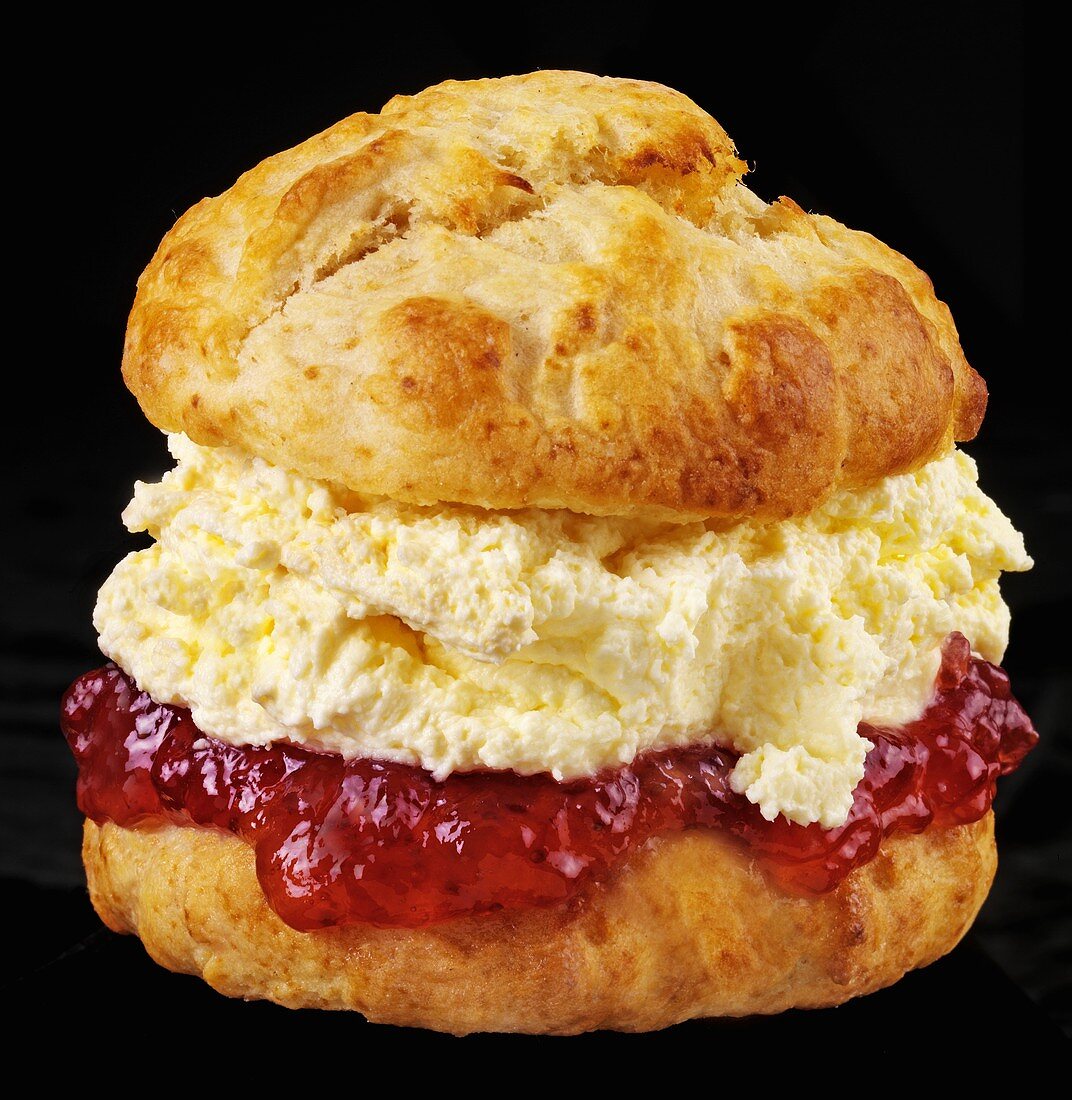 Scone with jam and cream against black background