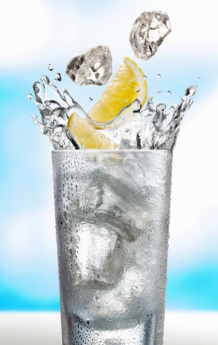 Eiswürfel und Zitronenschnitze fallen in ein Wasserglas
