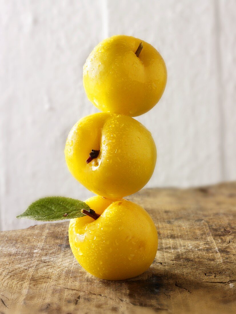 Three yellow plums, in a pile, one on top of the other