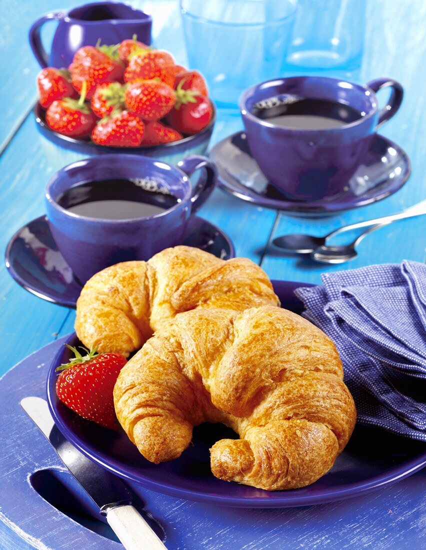 Two croissants, two cups of coffee and fresh strawberries