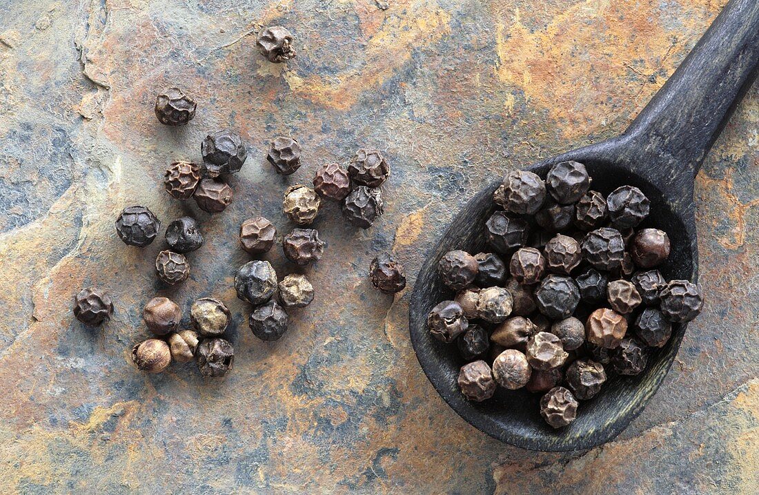 Black peppercorns in and beside wooden spoon