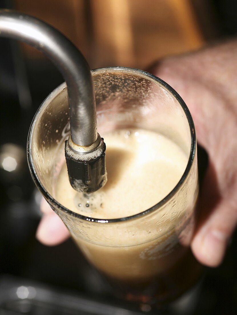 Someone filling a glass with dark beer from a tap