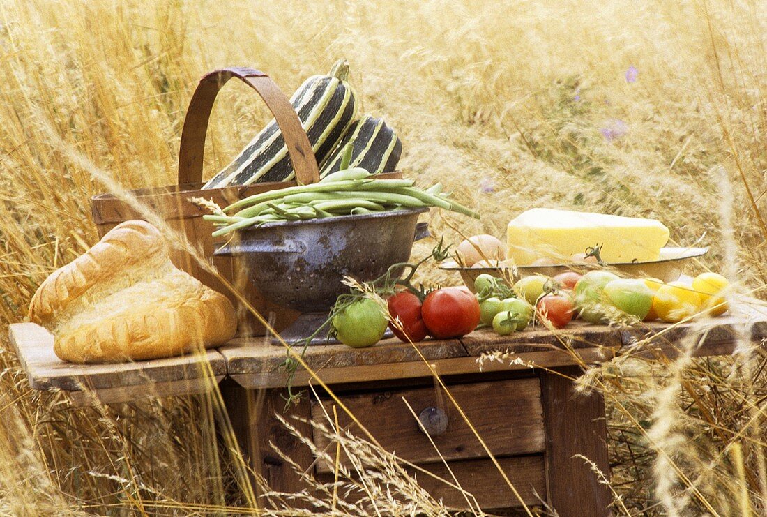 Tisch im Getreidefeld mit Brot, Tomaten, Kürbis und Käse