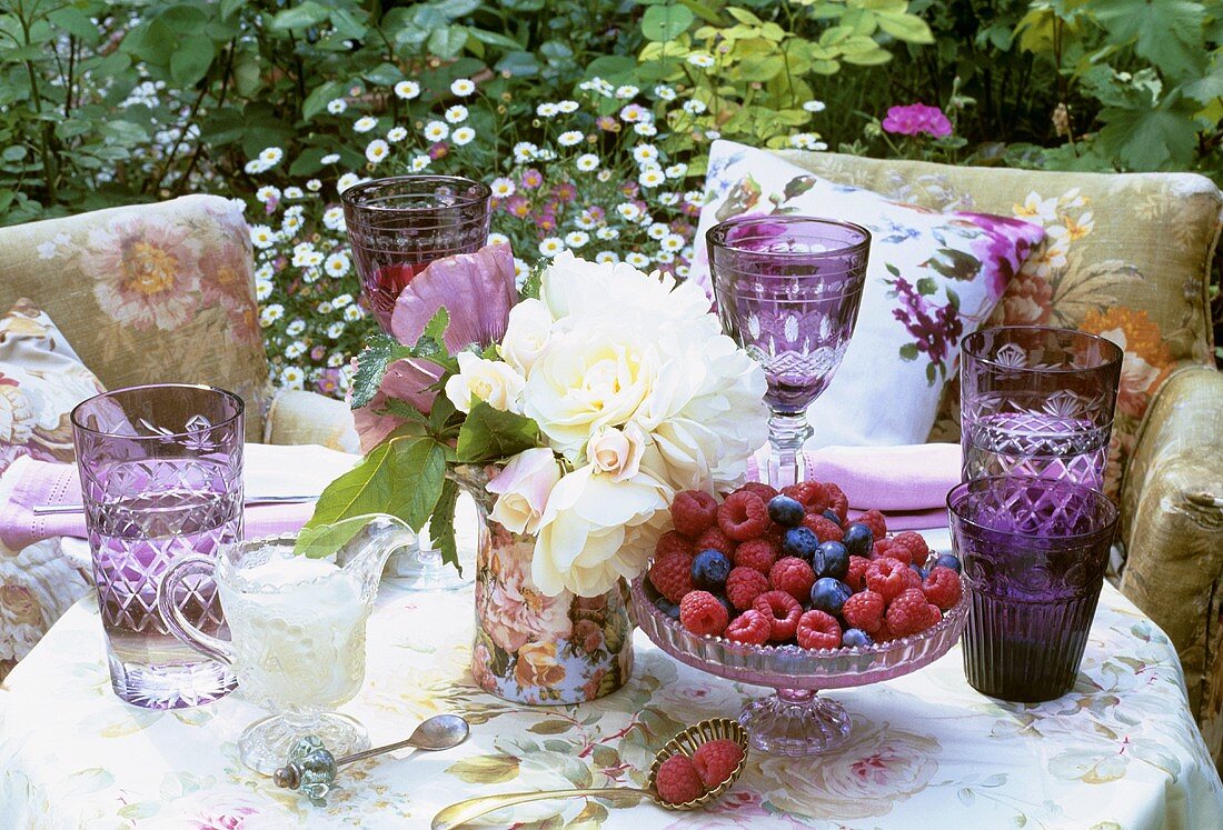 Tisch mit frischen Beeren, Rosen und Gläsern im Freien