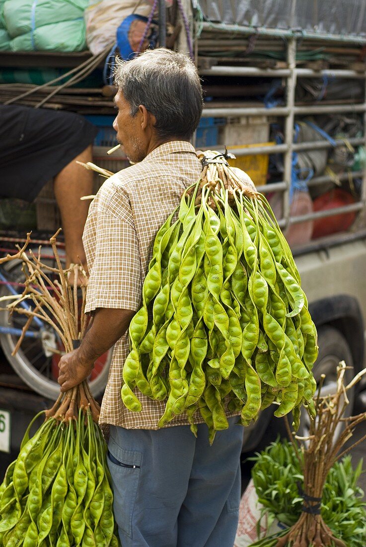 Mann mit Petaibohnen auf dem Markt in Thailand