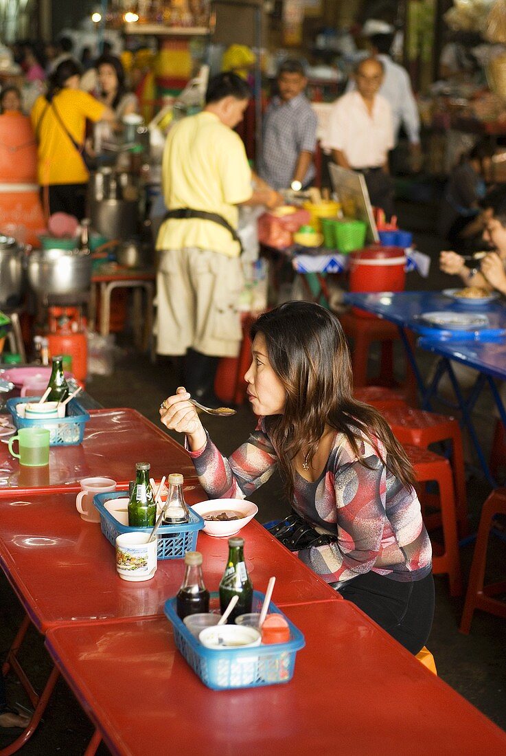 Frau beim Essen auf einem Markt in Thailand