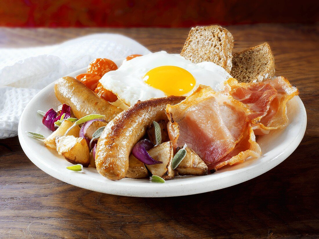 Englisches Frühstück mit Würstchen, Speck, Ei und Gemüse