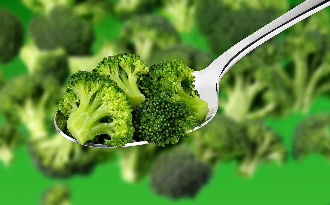 Broccoli florets on a spoon and in background