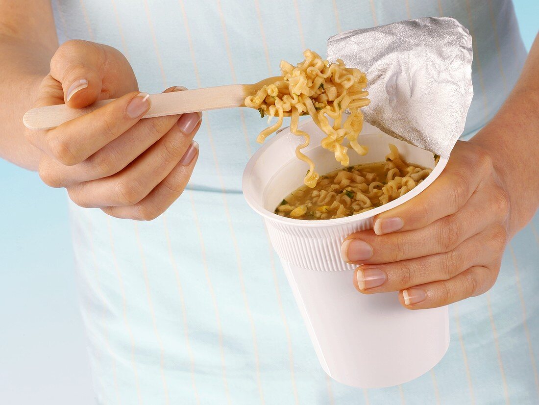 Hands holding instant noodles in plastic pot