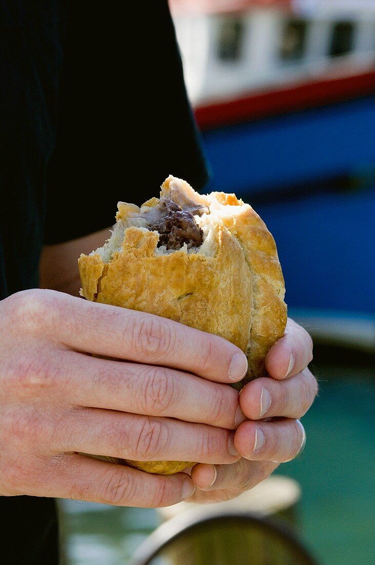 Hands holding a partly eaten Cornish pasty