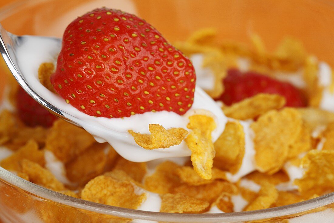 A strawberry with yoghurt and cornflakes on a spoon