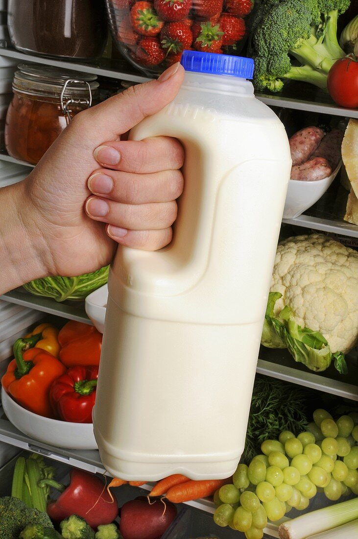 Hand hält eine Flasche Milch vor geöffnetem Kühlschrank