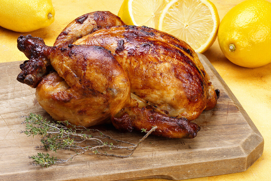 A whole grilled chicken with lemons and sprig of thyme