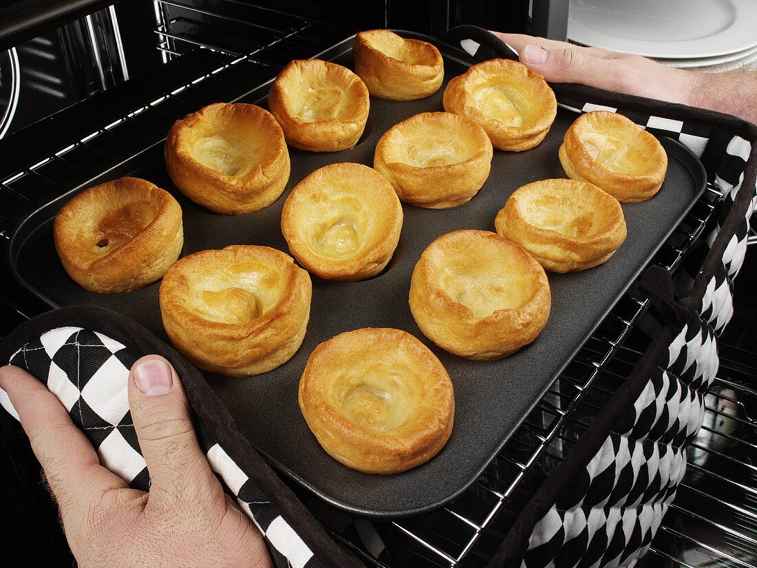 Mann holt gebackene Yorkshire Puddings aus dem Ofen