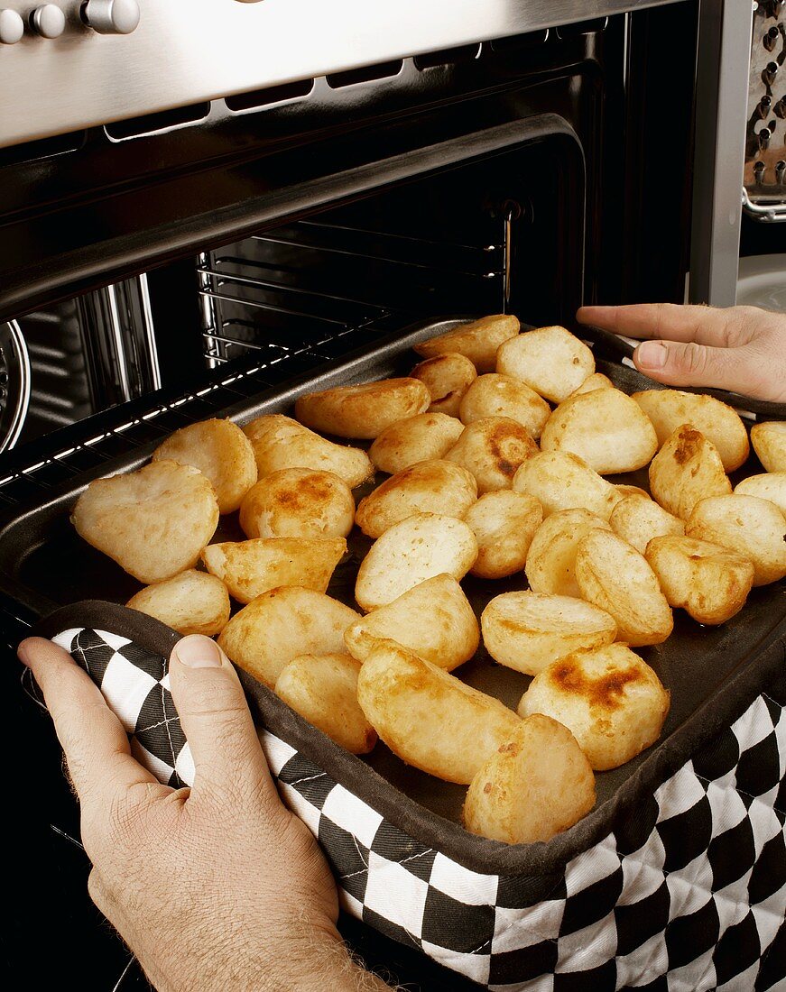 Mann holt Blechkartoffeln aus dem Ofen