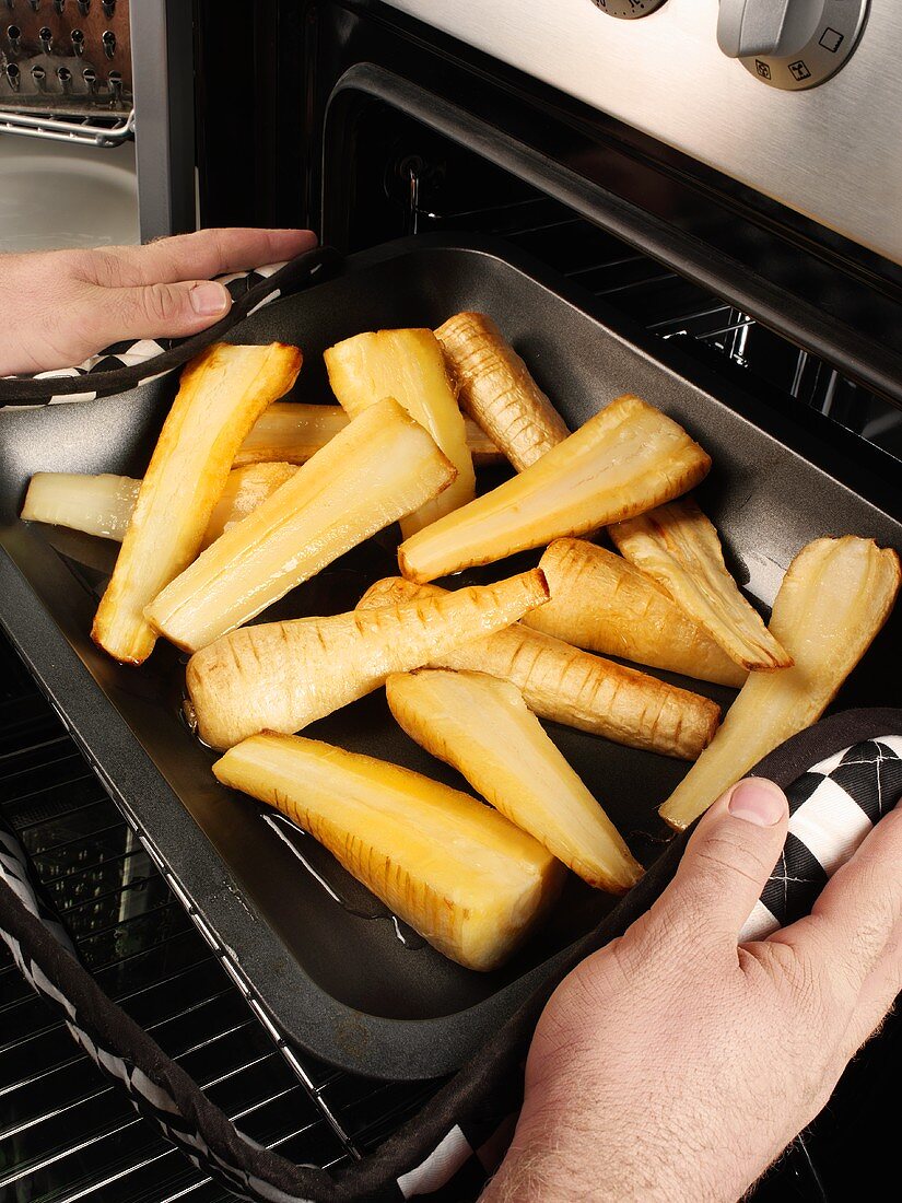Man taking roasted, halved parsnips out of the oven