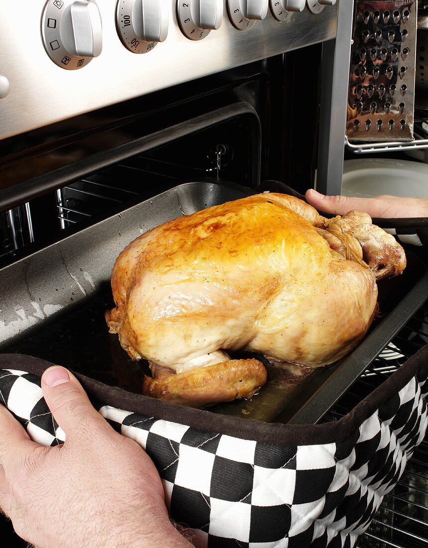Man taking a whole chicken out of the oven