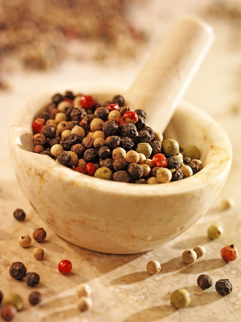 Mixed peppercorns in and beside a mortar