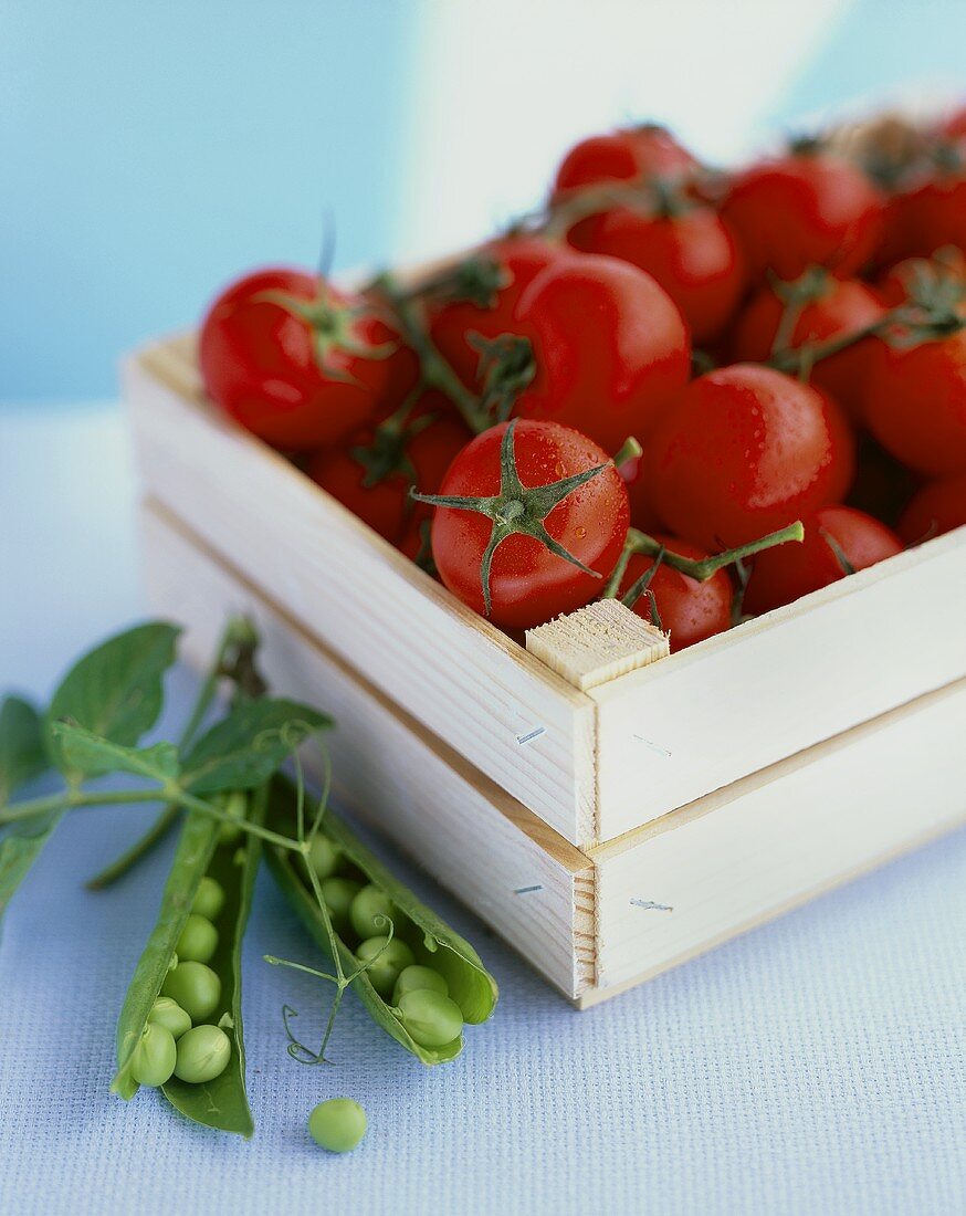 Cocktail tomatoes in a wooden crate and peas in pods