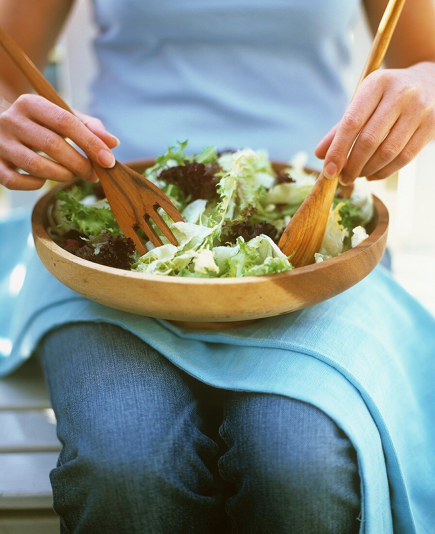 Frau vermengt Blattsalate in einer Salatschüssel