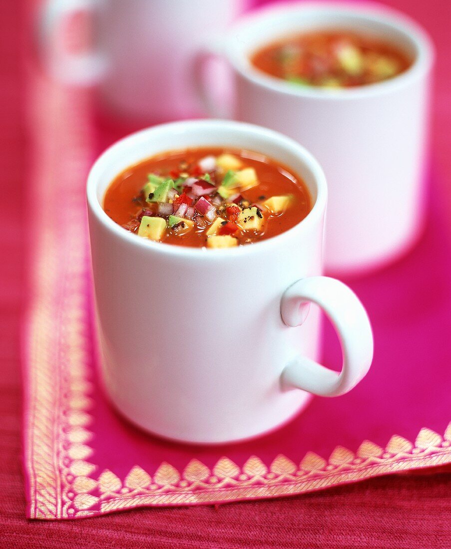 Tomato soup with avocado and diced onion in three mugs