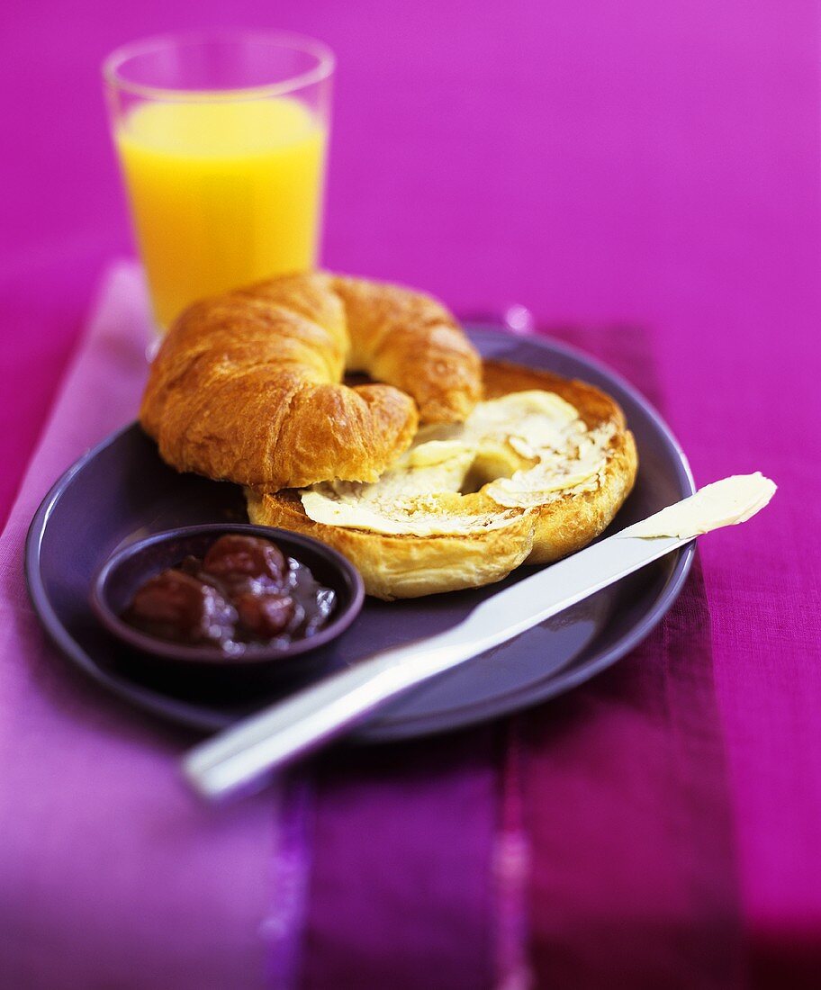 Croissant mit Butter, Konfitüre und einem Glas Orangensaft