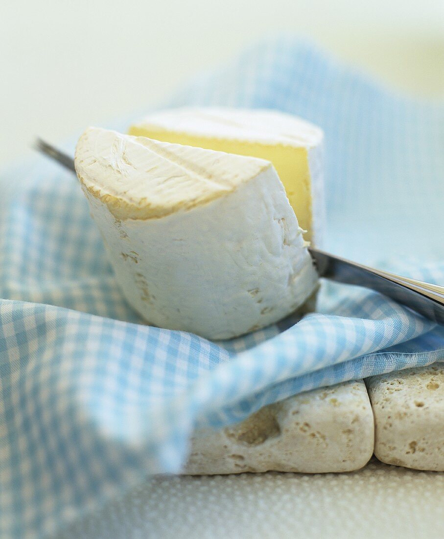 A cheese cut in half on a cloth with a knife