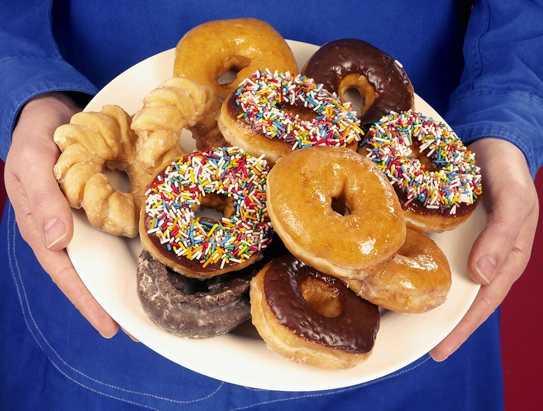 Hände halten Teller mit verschiedenen Doughnuts