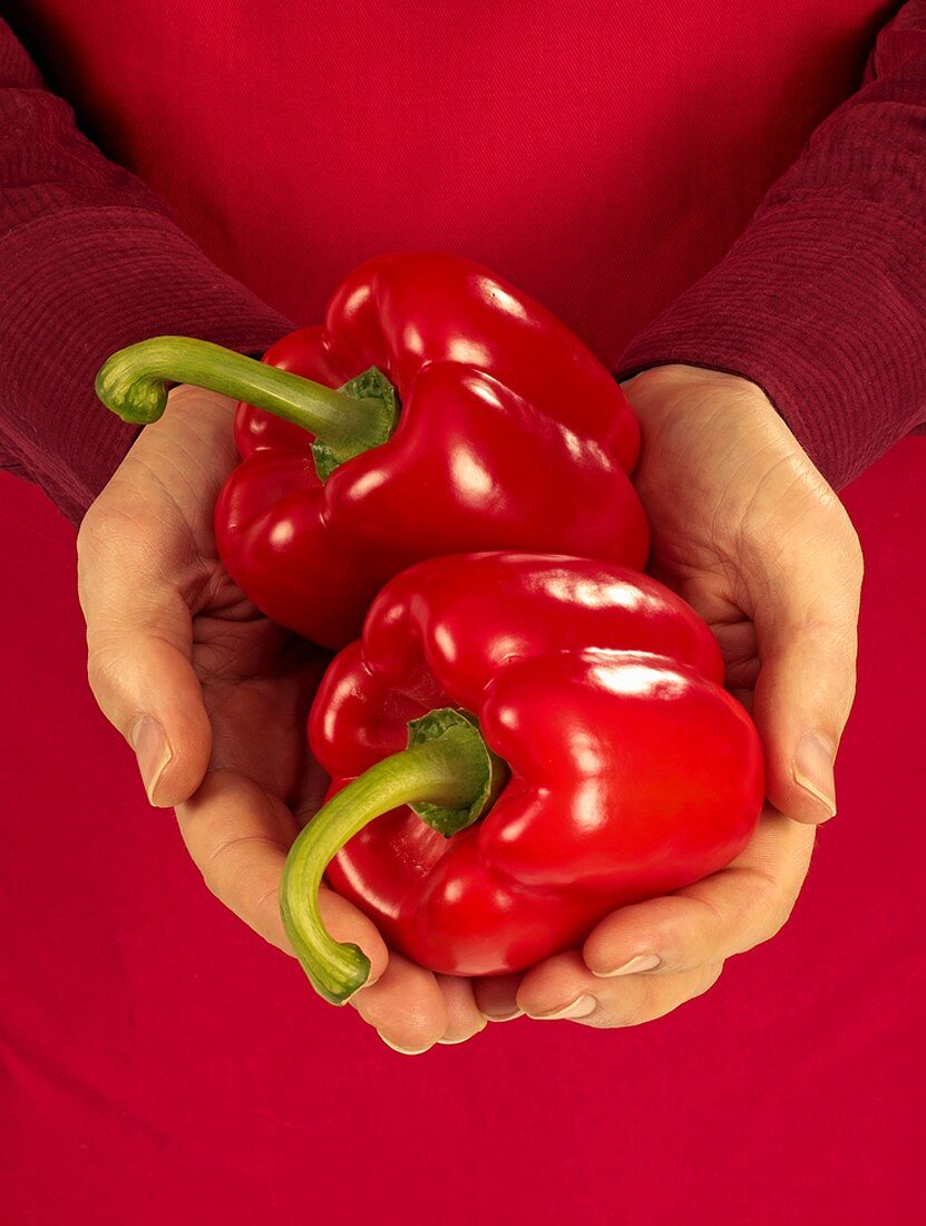 Hands holding two red peppers