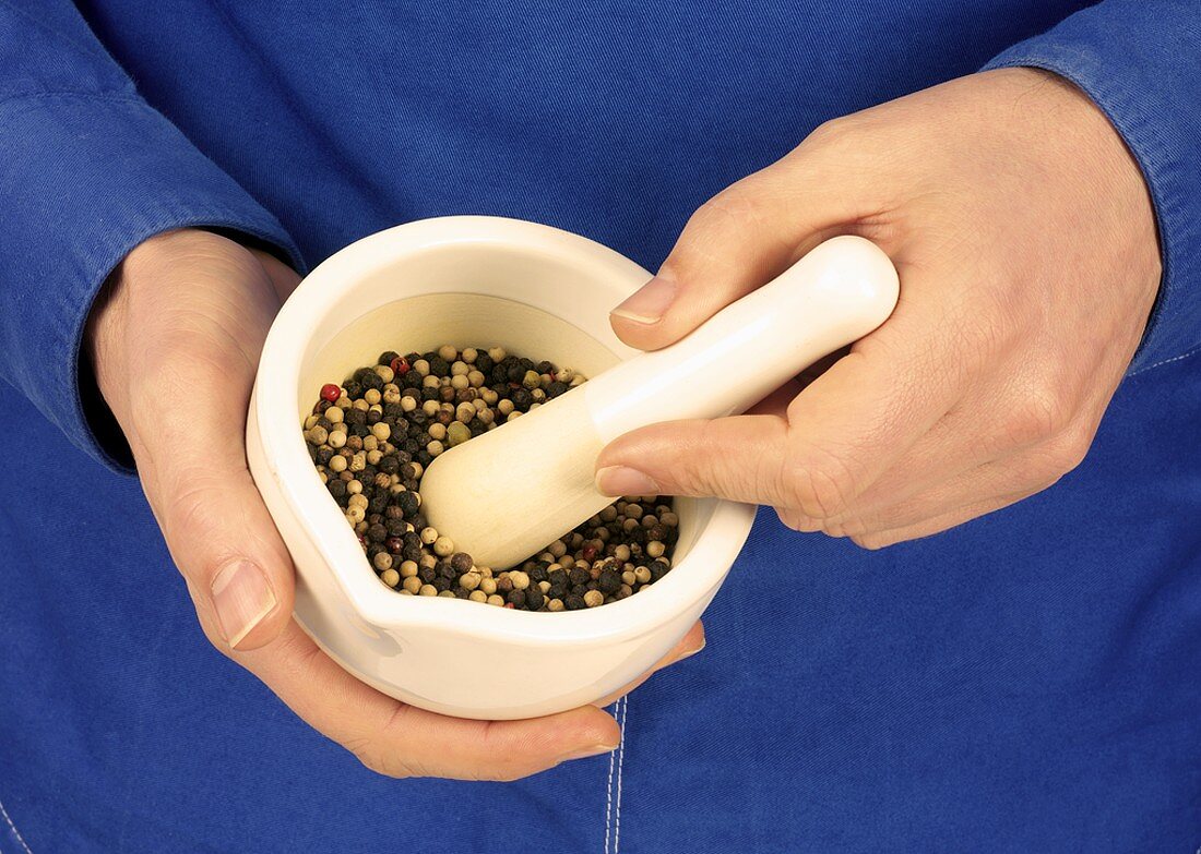 Hands holding mortar containing peppercorns