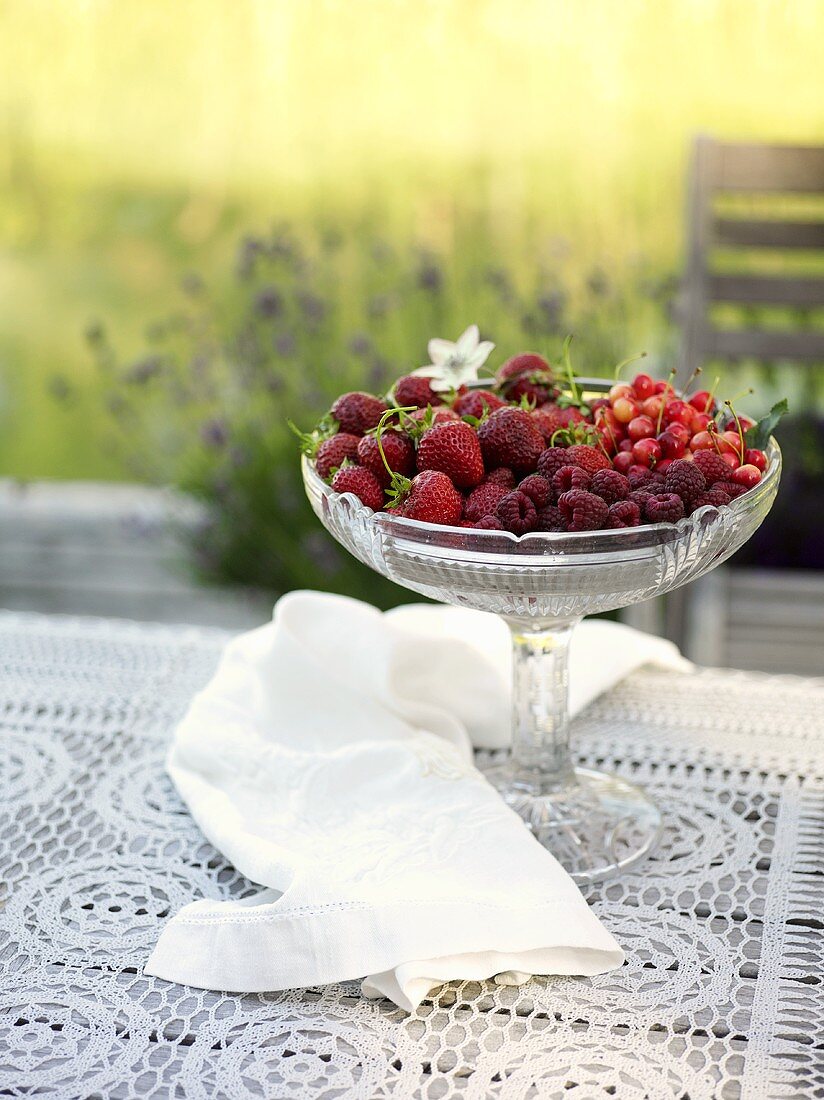 Beeren und Kirschen in Kristallschale auf Tisch im Freien