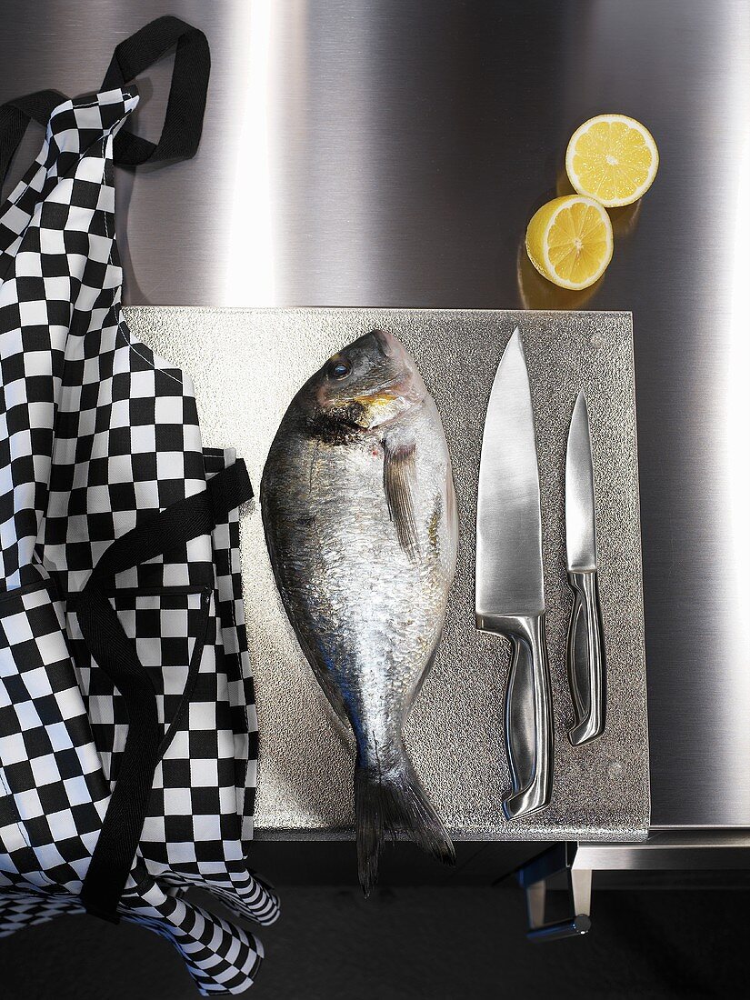Sea bream, kitchen knives and apron on chopping board