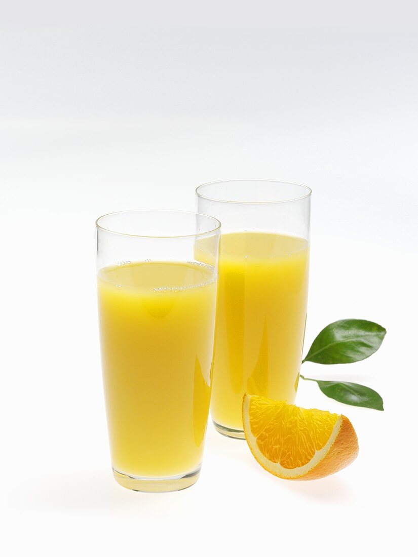 Two glasses of orange juice, wedge of orange and leaves