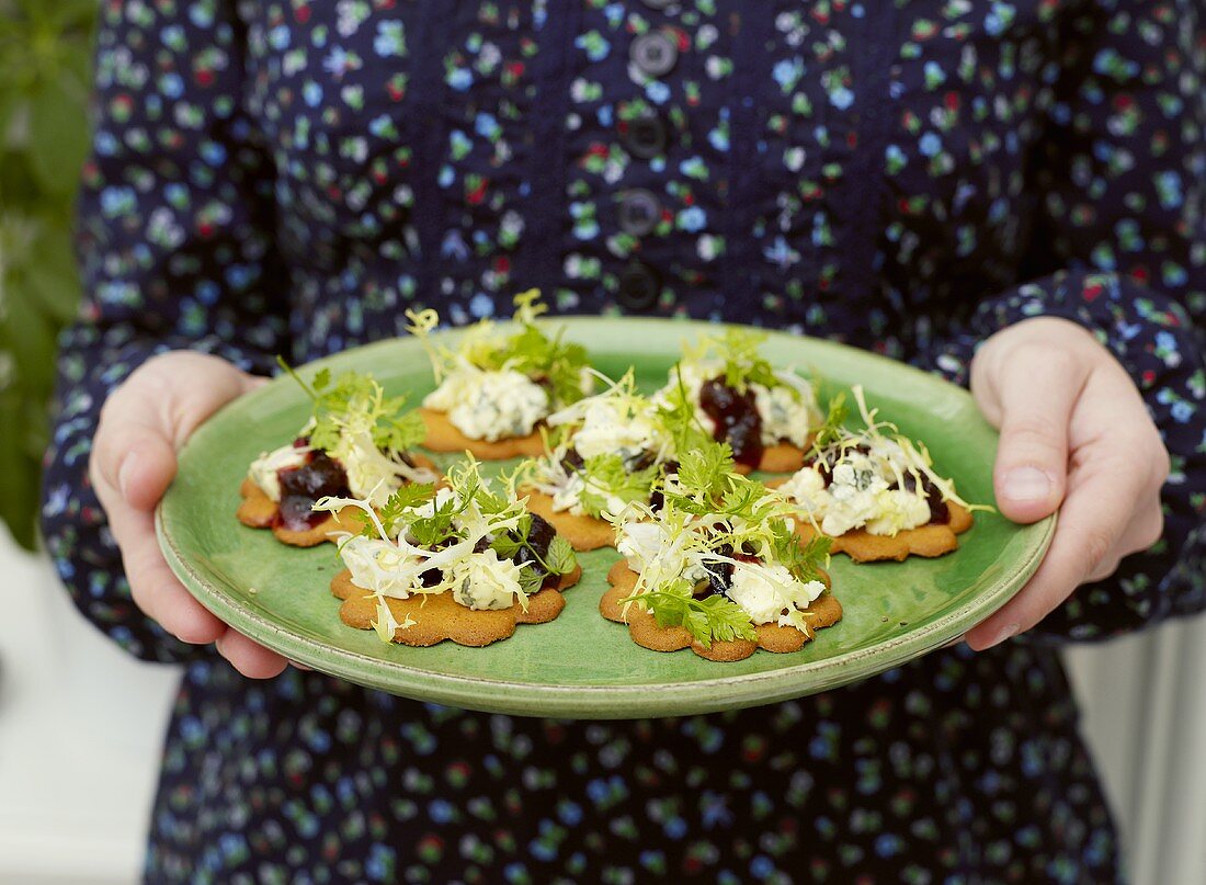 Woman holding plate of ginger biscuits with savoury toppings