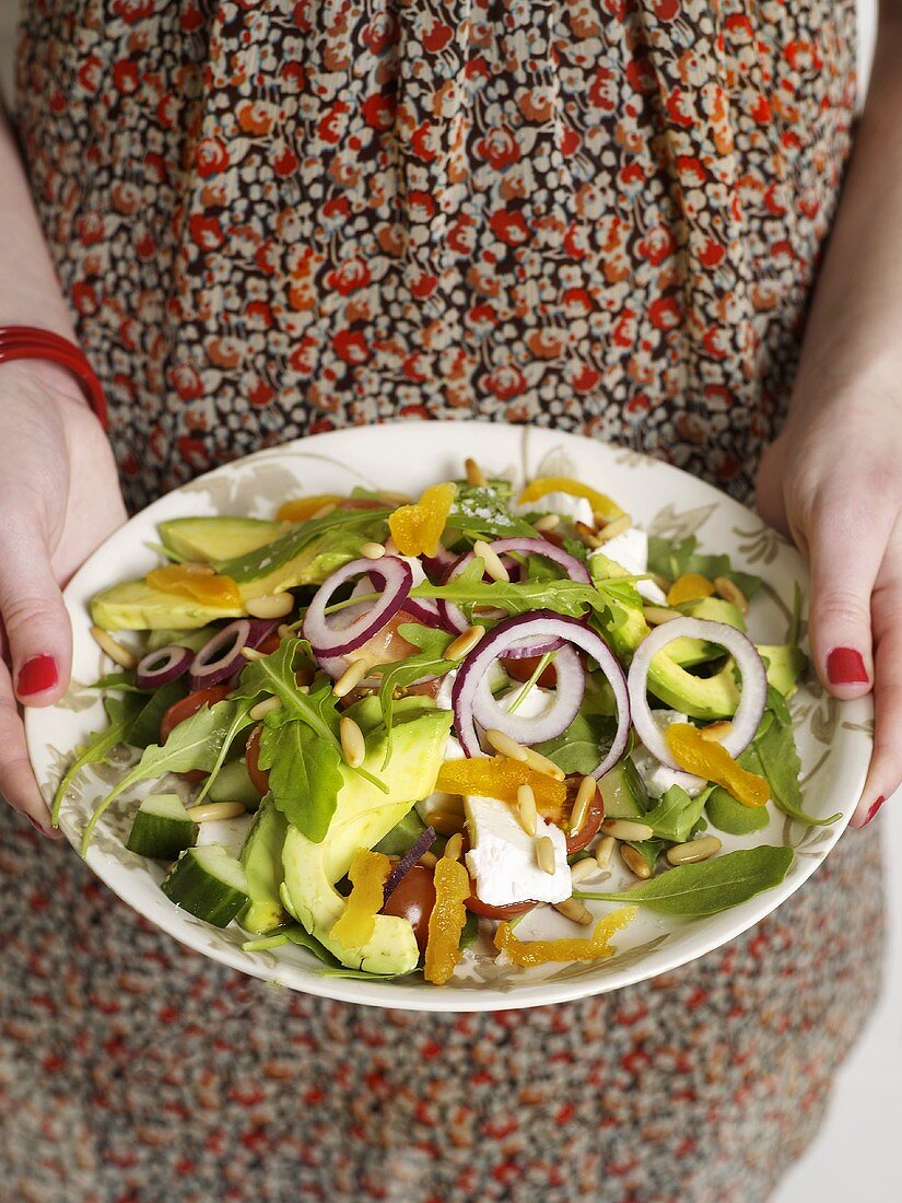 Frau hält Salatteller mit Ziegenkäse und Trockenfrüchten