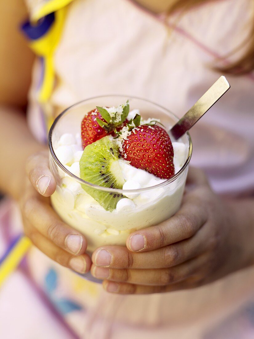 Child's hands holding soft vanilla ice cream with fruit